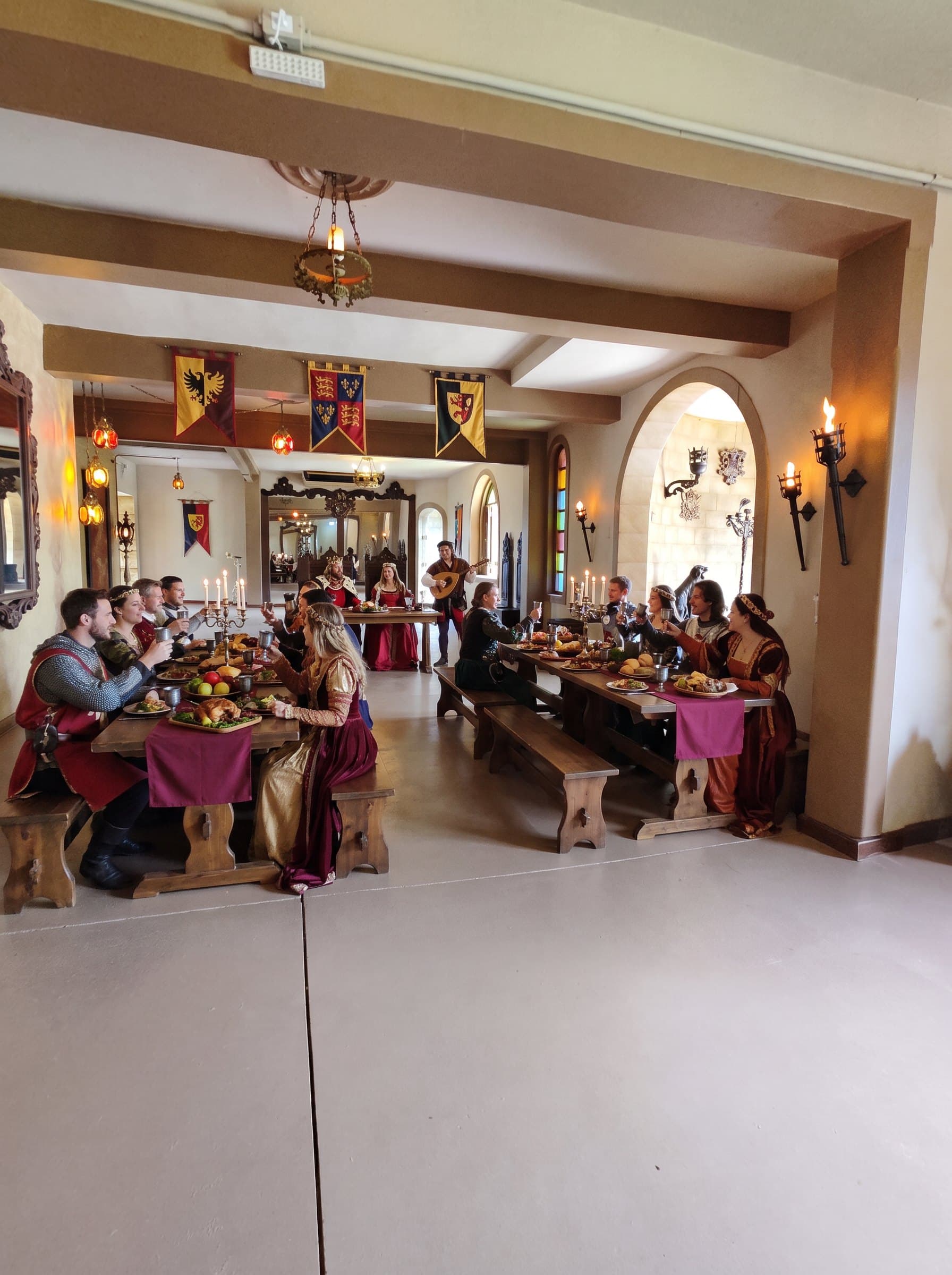 Salão de banquete com mesas longas de madeira, estandartes heráldicos e tochas nas paredes